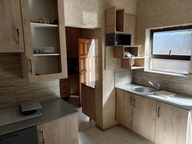 A compact kitchen featuring light wood-look cabinetry, tiled backsplash, and a stainless steel sink, requiring cosmetic updates to improve the overall finish.