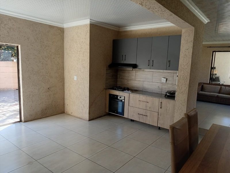 Compact kitchen area featuring modern two-tone cabinetry, built-in oven and gas hob, set against textured walls with neutral floor tiling.