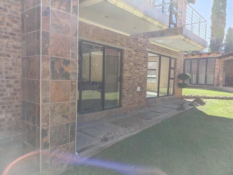 Rear view of a face brick house featuring slate tile accents, large sliding glass doors, and an upper-level balcony with a stainless steel balustrade.