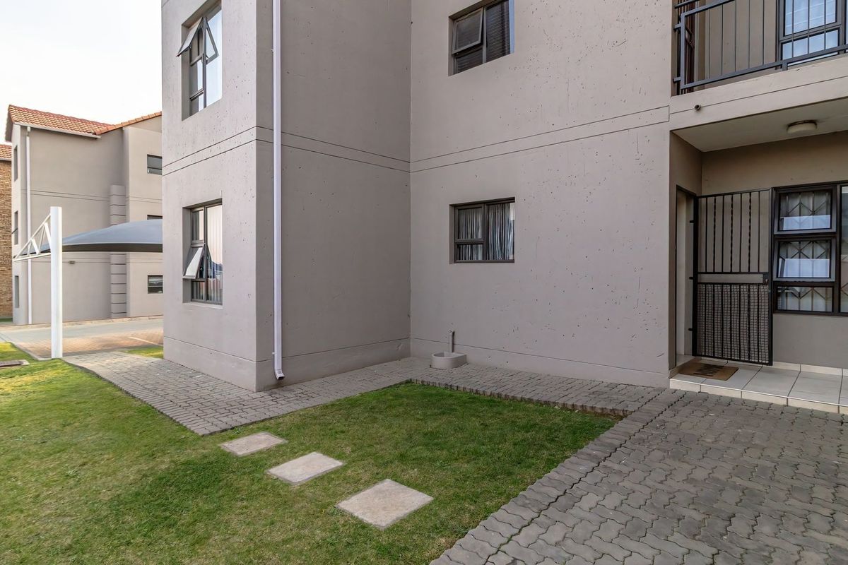 A view of the apartment exterior featuring a paved walkway, small lawn area, and secure entrance with a metal security gate.