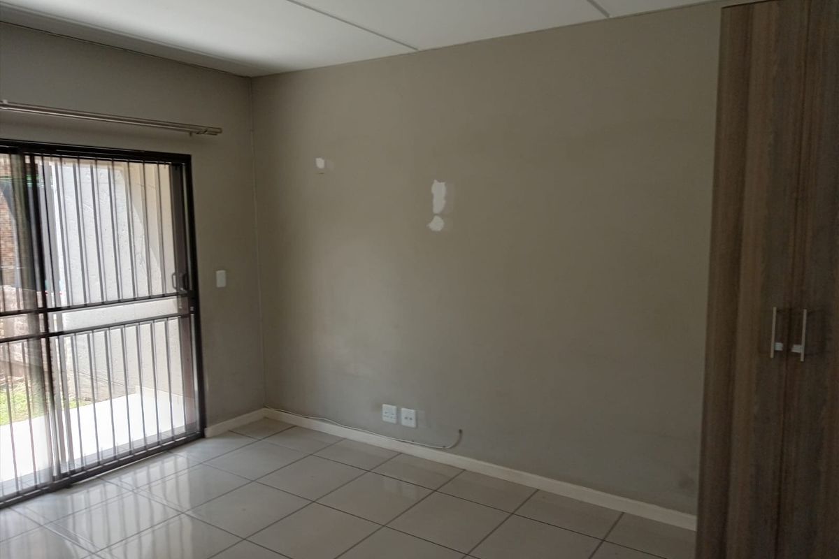 An empty bedroom featuring tiled flooring, a built-in wardrobe, and a sliding glass door with a security gate leading to the exterior.