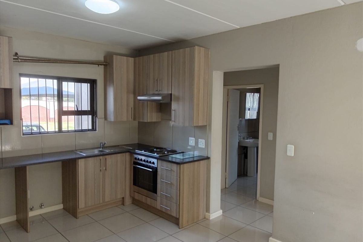 A clean, functional kitchen featuring modern wood-look cabinetry, built-in oven and hob, tiled flooring, and a window with security bars.