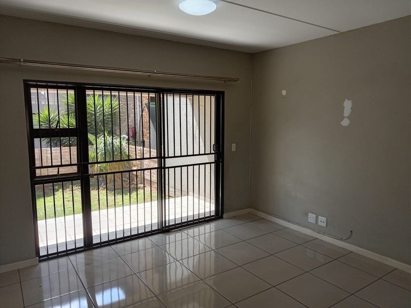 An empty living room featuring tiled flooring and a sliding glass door with security bars, providing direct access to an outdoor patio area.