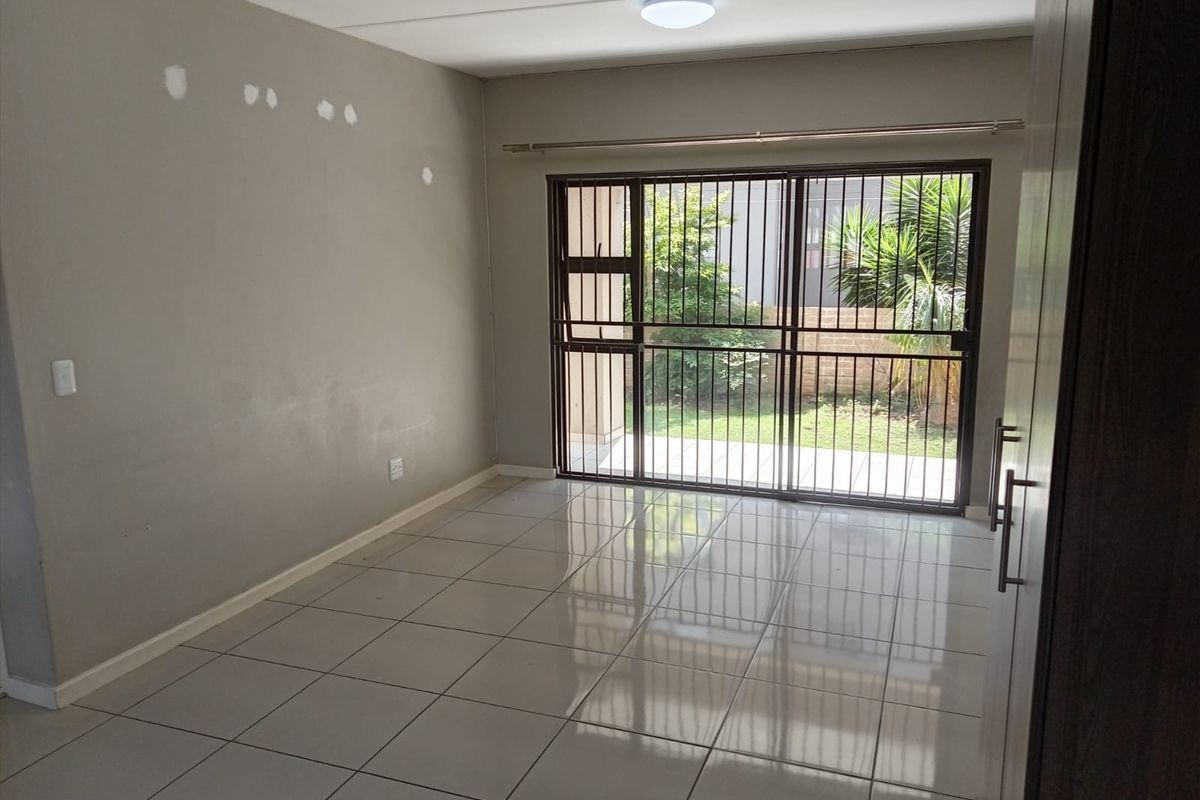An empty living room featuring tiled flooring and a sliding glass door with security gate, providing direct access to the outdoor area.