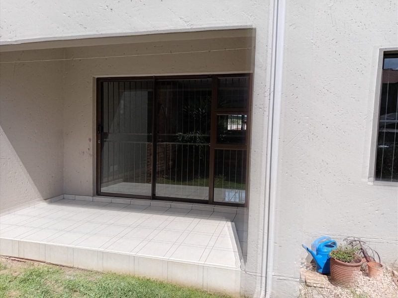 A covered patio area featuring tiled flooring and a sliding glass door with security bars, providing direct access to the exterior.