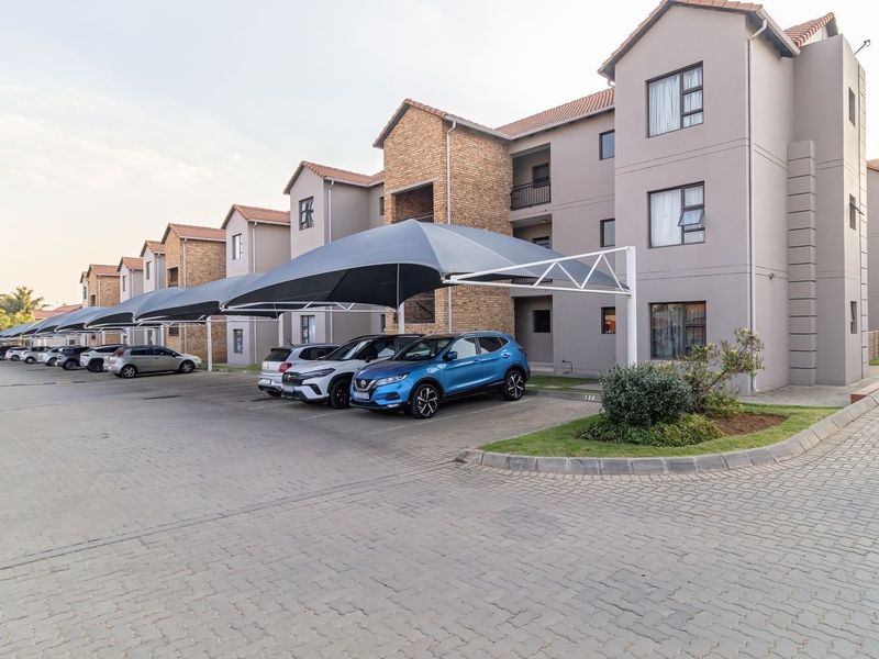 Exterior view of an apartment complex featuring paved parking areas with shade cloth carports and well-maintained building facades.