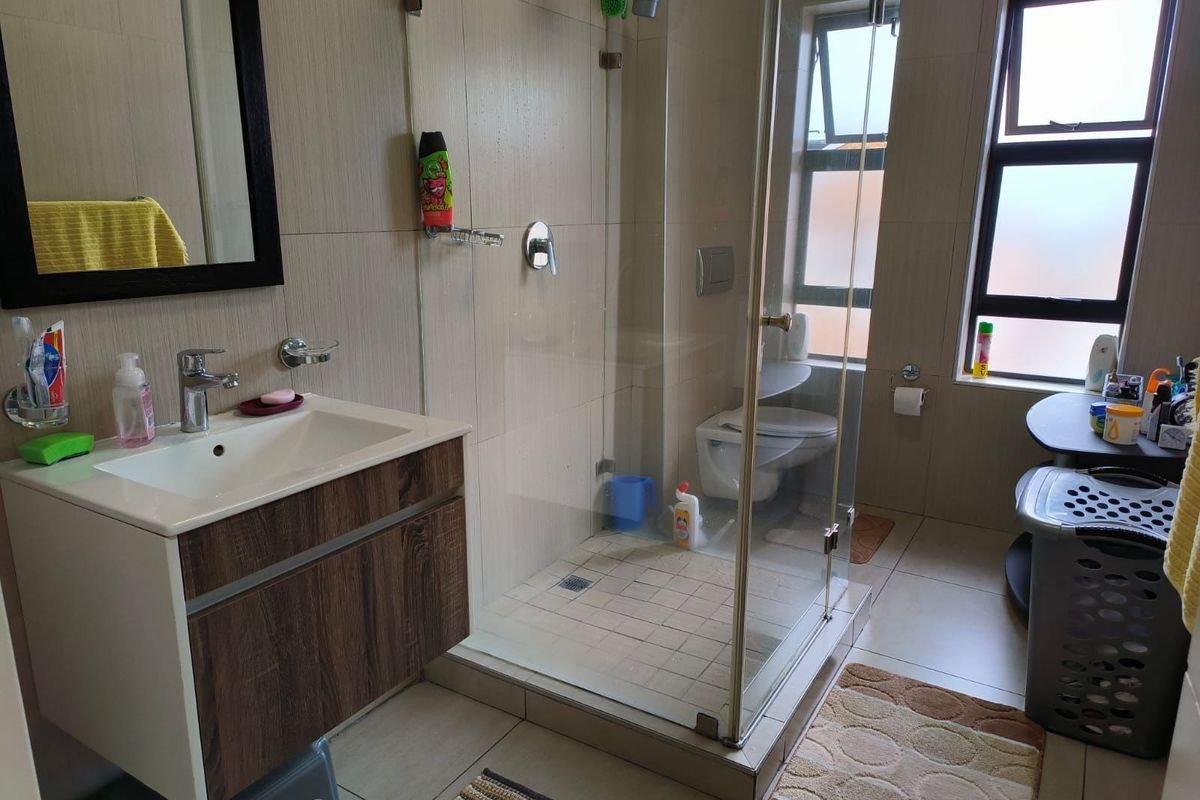 A modern bathroom featuring a wall-mounted vanity, a glass-enclosed shower, and a toilet with a window for natural light.
