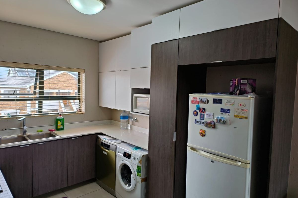 A functional kitchen featuring built-in cabinetry, integrated appliance spaces, a double sink, and a window with fitted blinds.
