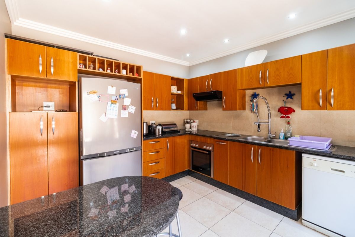 A functional kitchen featuring wooden cabinetry, granite countertops, a built-in oven, extractor fan, and tiled flooring.
