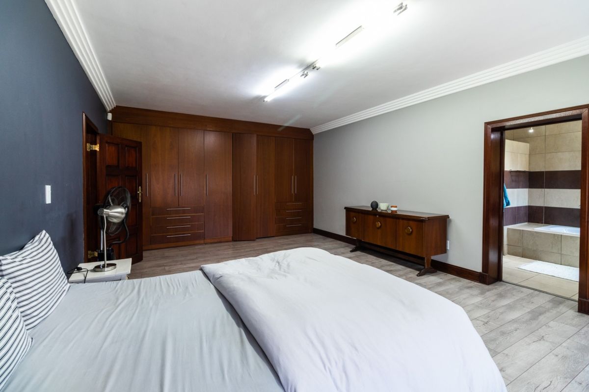 Spacious bedroom featuring extensive built-in wooden cabinetry, laminate flooring, crown molding, and an en-suite bathroom access.