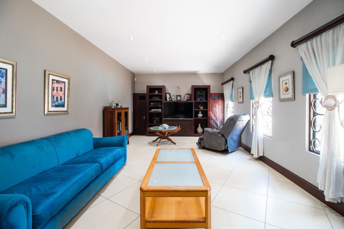 A spacious living room featuring neutral tiled flooring, recessed ceiling lighting, and a large built-in wooden media unit.