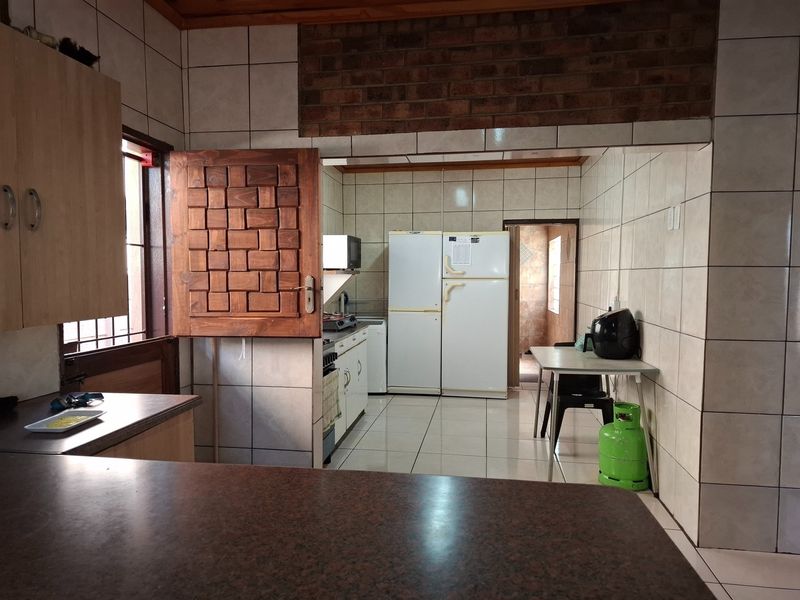 A functional kitchen featuring tiled walls, built-in cabinetry, and a gas stove, with an open-plan layout and an exposed brick accent wall.