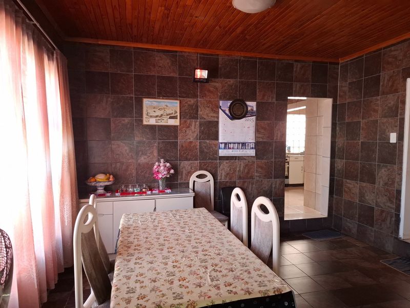 Dining room featuring dark tiled walls, tiled flooring, and a timber-clad ceiling, with an open doorway leading to the kitchen area.