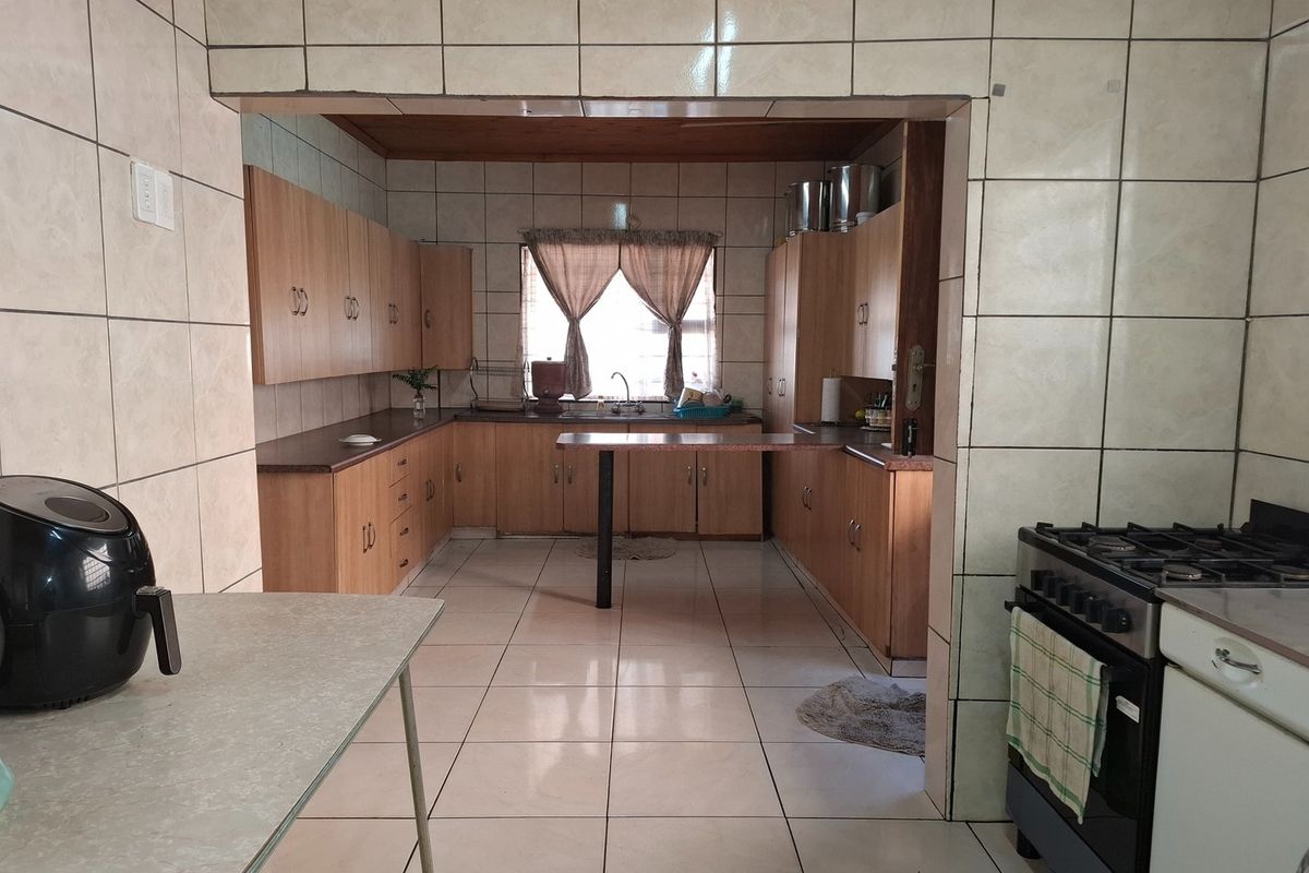 A functional kitchen featuring extensive built-in cabinetry, laminate countertops, a double sink, and a freestanding gas stove, finished with full-height wall tiling.