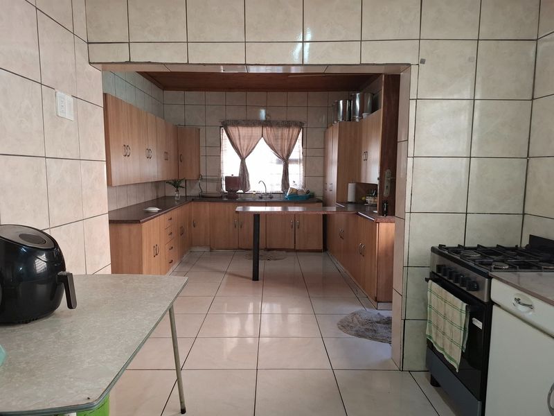 A functional kitchen featuring extensive built-in cabinetry, laminate countertops, a double sink, and a freestanding gas stove, finished with full-height wall tiling.