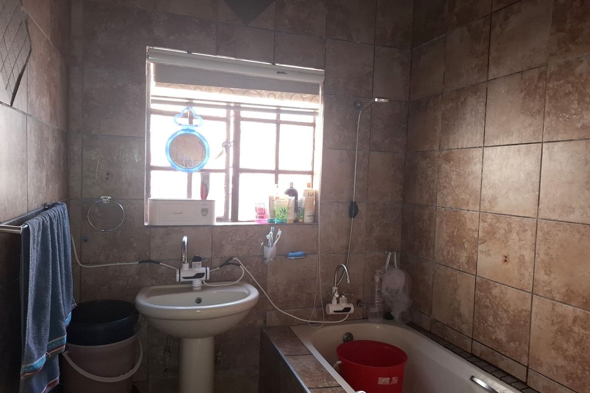 A dated bathroom featuring a pedestal basin, built-in bathtub, and full-height wall tiling. The space requires cosmetic updates to improve its overall condition.