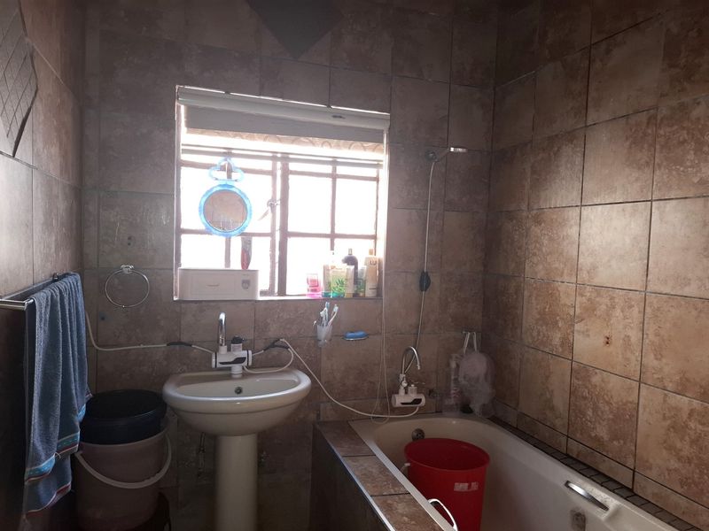 A dated bathroom featuring a pedestal basin, built-in bathtub, and full-height wall tiling. The space requires cosmetic updates to improve its overall condition.