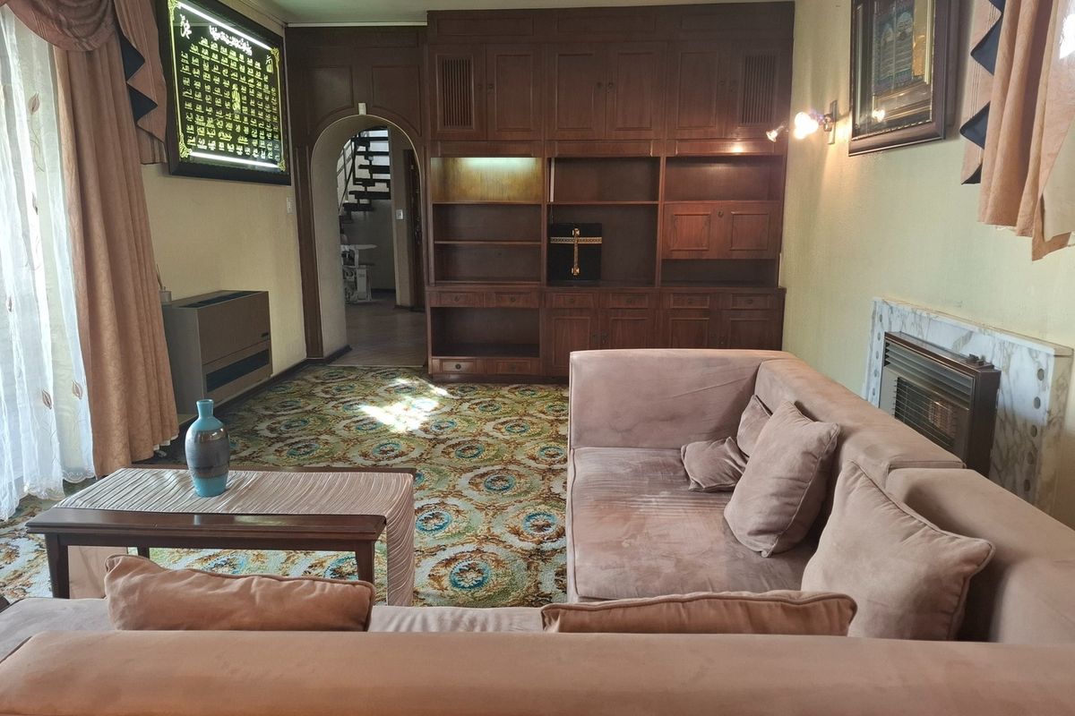 A living room featuring built-in wooden cabinetry, a fireplace with a marble surround, and an arched entryway leading to a staircase.