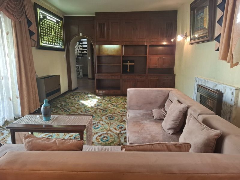 A living room featuring built-in wooden cabinetry, a fireplace with a marble surround, and an arched entryway leading to a staircase.
