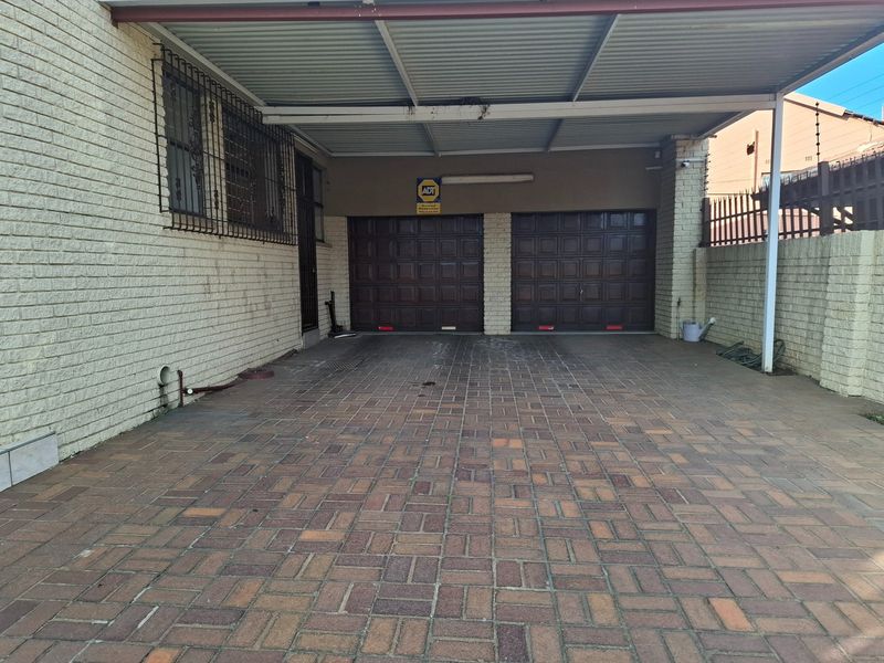 A double garage with a paved driveway and an attached carport, featuring brick exterior walls and security bars on the windows.