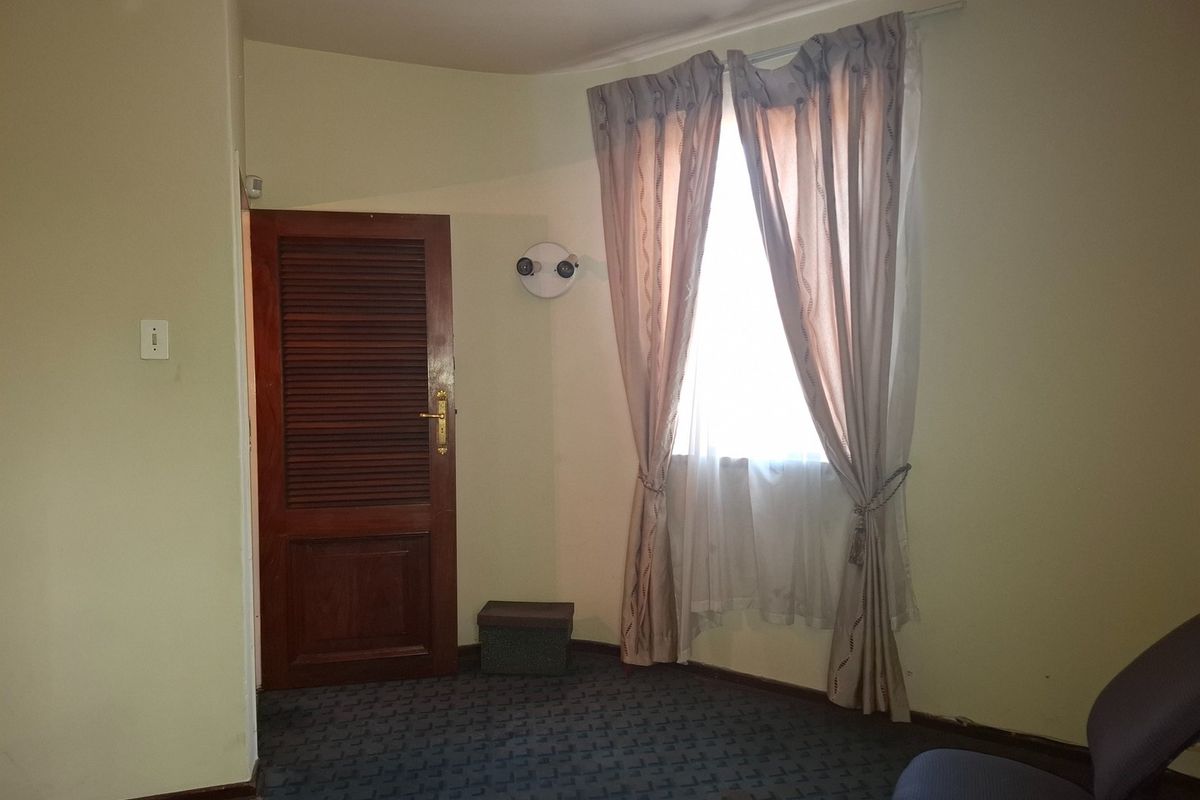 A bedroom featuring a louvered timber door, wall-mounted lighting, and carpeted flooring, offering a blank canvas for potential interior updates.