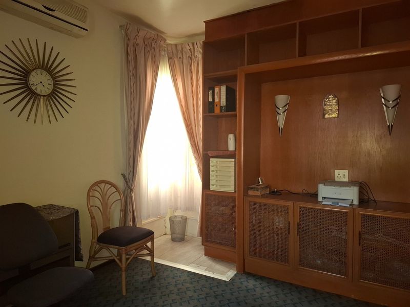A home office featuring extensive built-in wooden cabinetry, wall-mounted air conditioning, and classic wall sconces, providing functional storage and workspace.