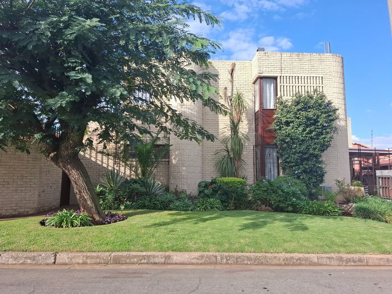 Front elevation of a multi-story brick house featuring distinctive curved architectural elements, security window bars, and a well-maintained front garden.