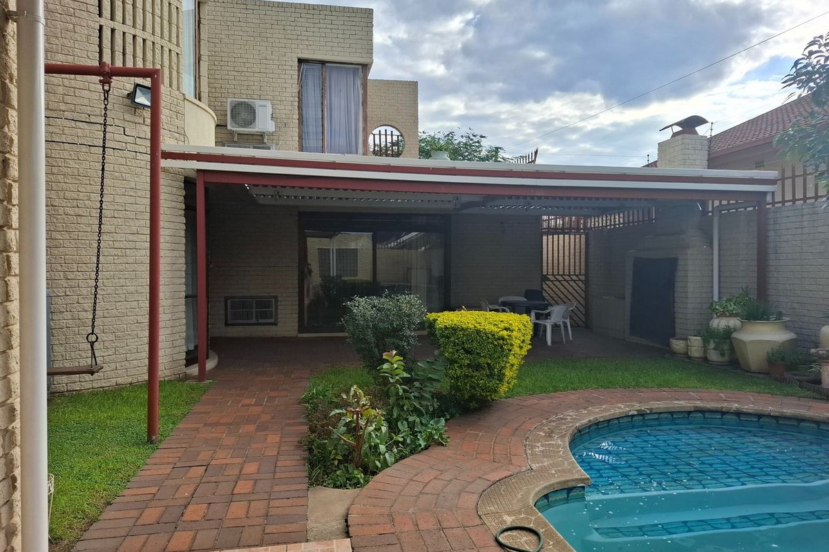 Rear exterior view featuring a swimming pool, brick-paved patio area, and a covered outdoor entertainment space with a built-in braai.