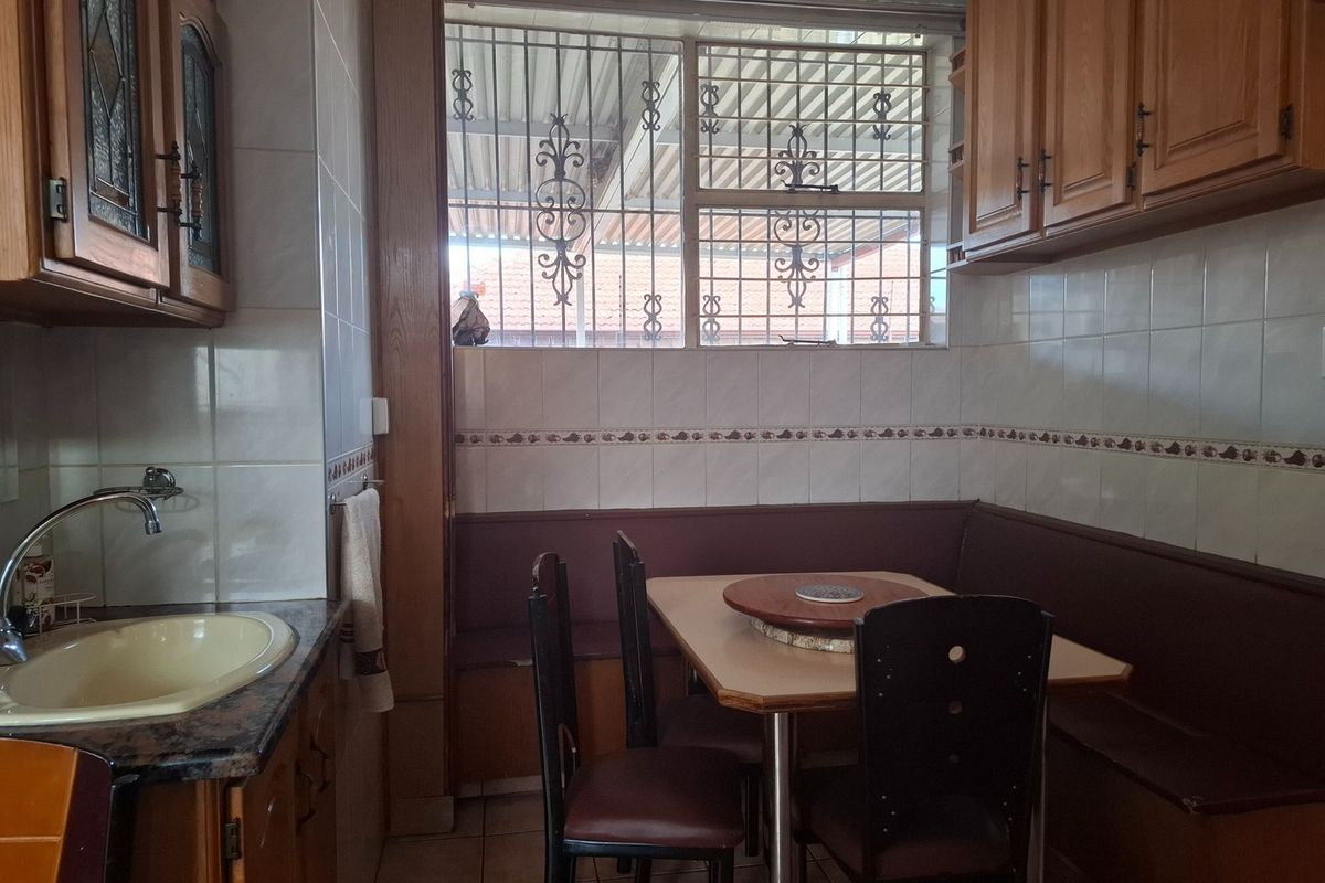 A functional kitchen area featuring built-in wooden cabinetry, a tiled backsplash, a sink, and a built-in bench seating area with security bars on the window.
