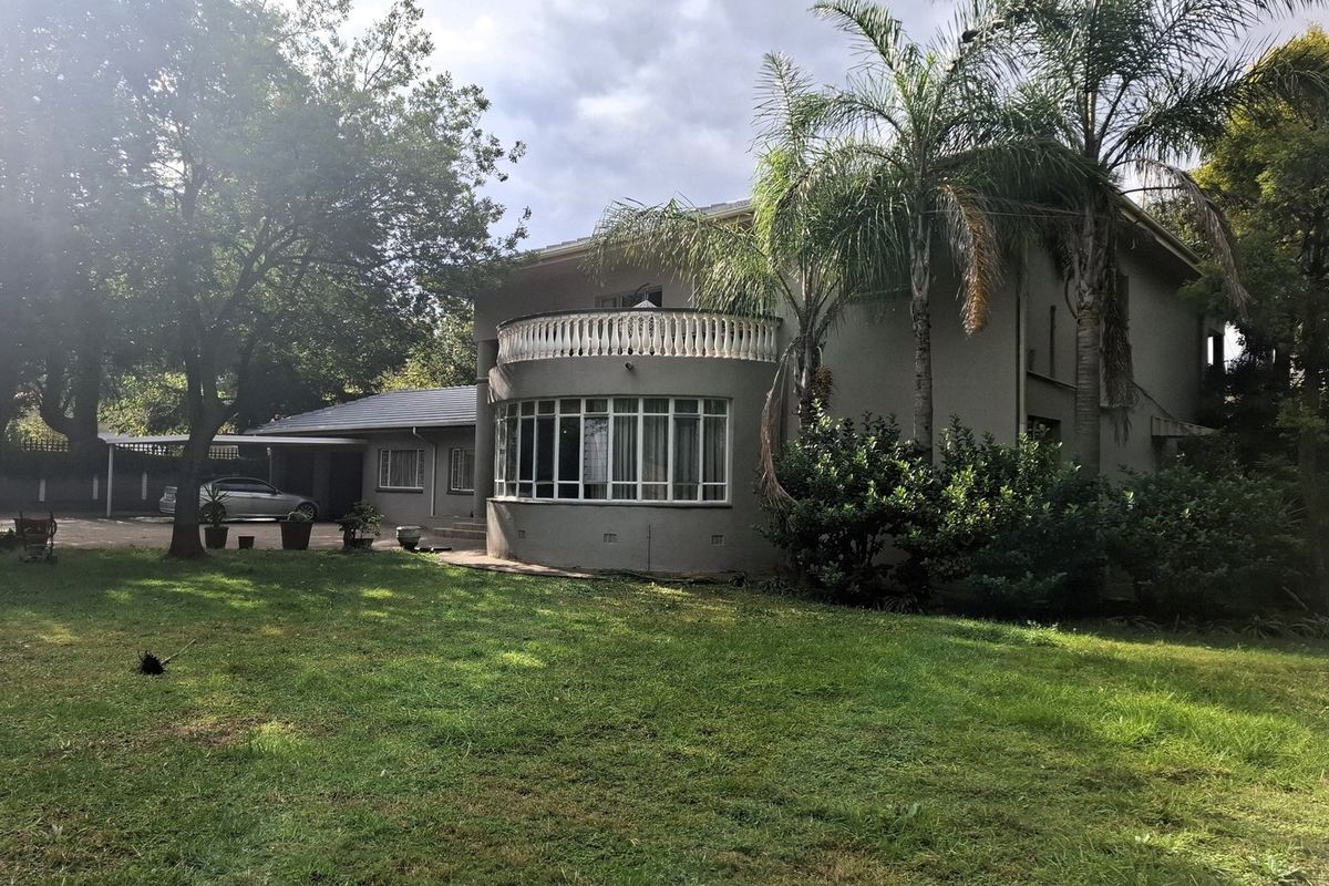 Rear view of the house featuring a curved balcony with balustrade, large garden, and attached carport area.