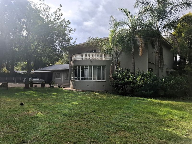 Rear view of the house featuring a curved balcony with balustrade, large garden, and attached carport area.