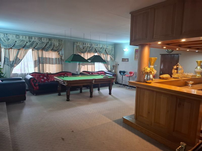 Spacious entertainment room featuring a built-in wooden bar, dedicated billiard area with overhead lighting, and neutral carpeting throughout.