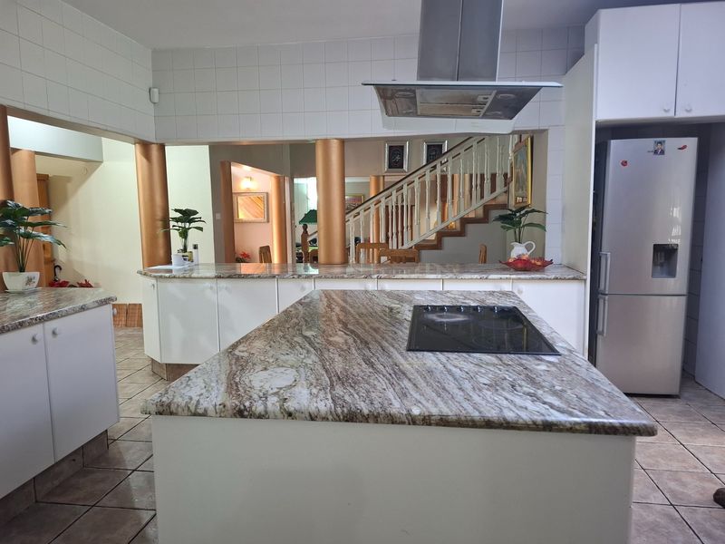 Spacious kitchen featuring a large granite-topped island with integrated cooktop, stainless steel extractor fan, and open-plan layout overlooking the staircase.