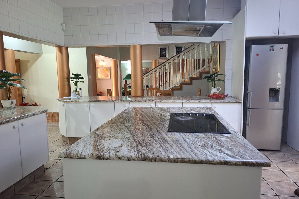 Spacious kitchen featuring a large granite-topped island with integrated cooktop, stainless steel extractor fan, and open-plan layout overlooking the staircase.