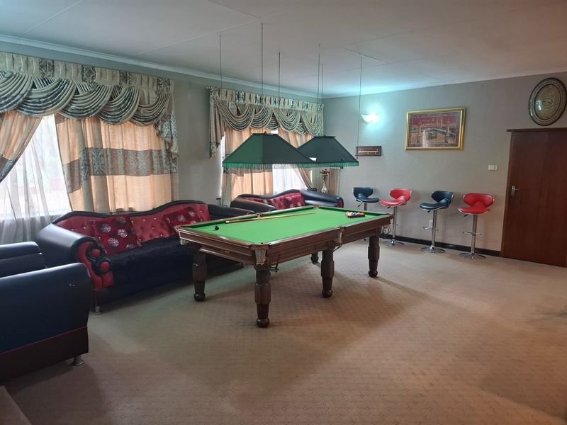 Spacious living area currently utilized as a games room, featuring neutral carpeting, cove lighting, and large windows with decorative pelmets.