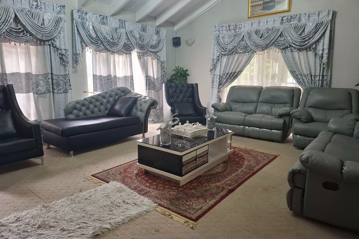 Spacious living room featuring a high vaulted ceiling with exposed beams and large windows with decorative drapery.