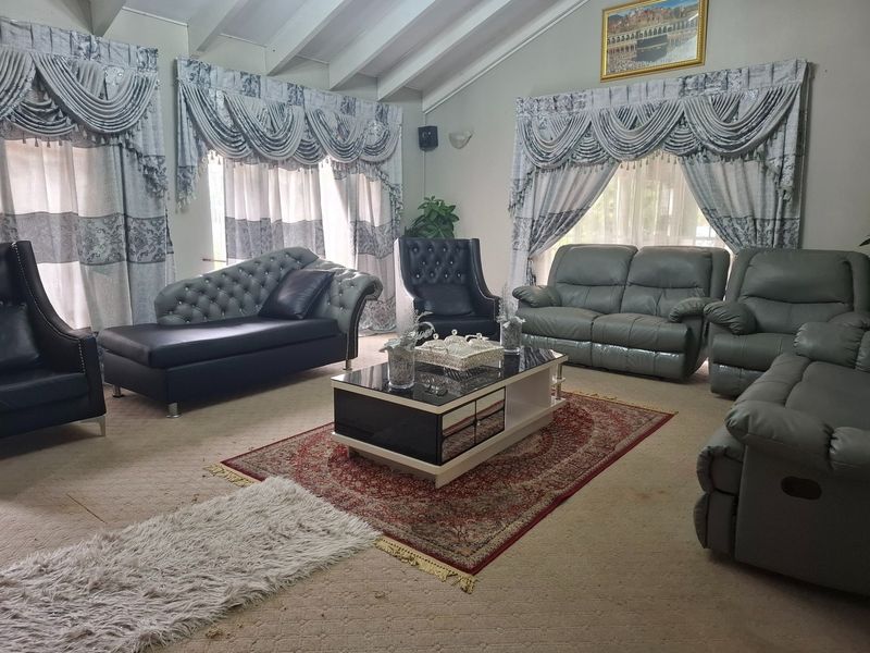 Spacious living room featuring a high vaulted ceiling with exposed beams and large windows with decorative drapery.