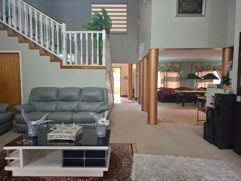 Spacious open-plan living area featuring a prominent staircase, decorative columns, and carpeted flooring, creating a versatile space for relaxation and entertainment.