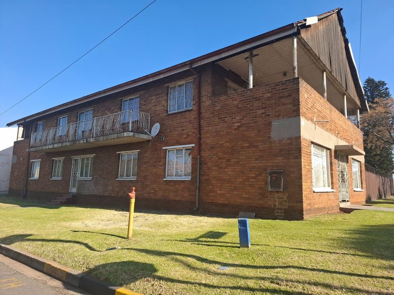 Exterior view of a two-story face brick residential building featuring a balcony, metal security gates, and steel window frames set on a grass verge.