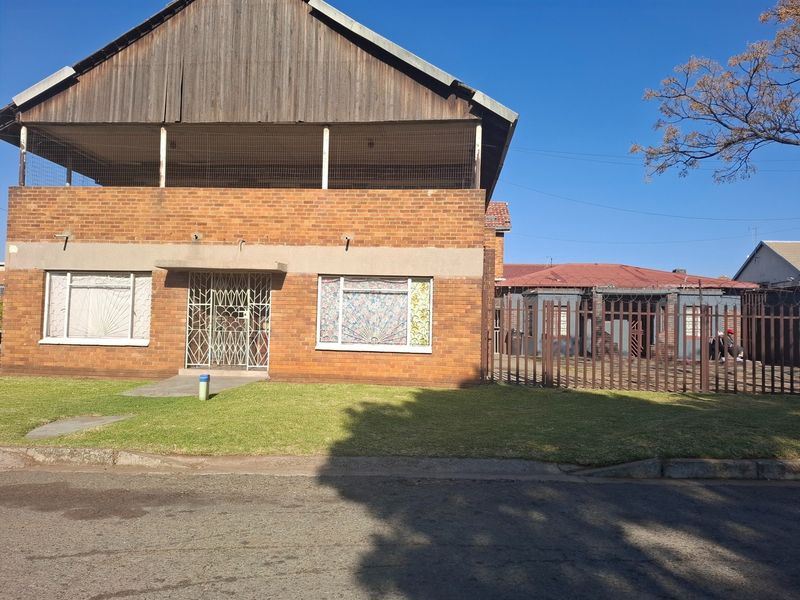 Front view of a two-story brick house featuring a timber-clad upper level, security gates, and a fenced front garden area.