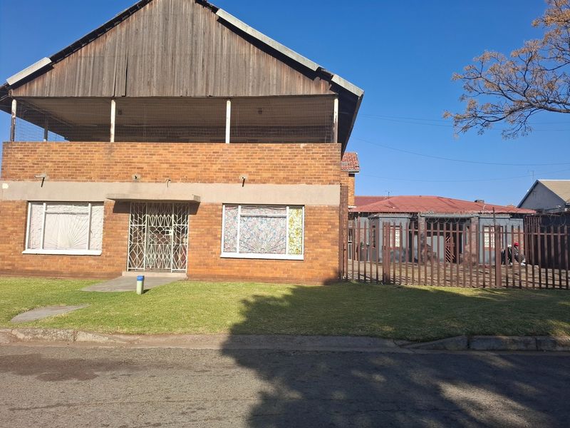 Front view of a two-story face brick house featuring a timber-clad upper gable, security gates, and metal perimeter fencing on a residential street.