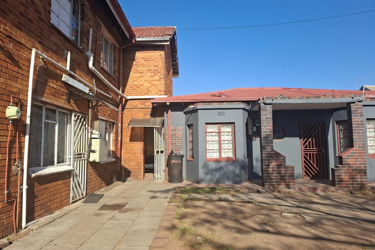 Rear exterior view of the property featuring a mix of face brick and painted walls, paved courtyard area, and secure metal entrance gates.