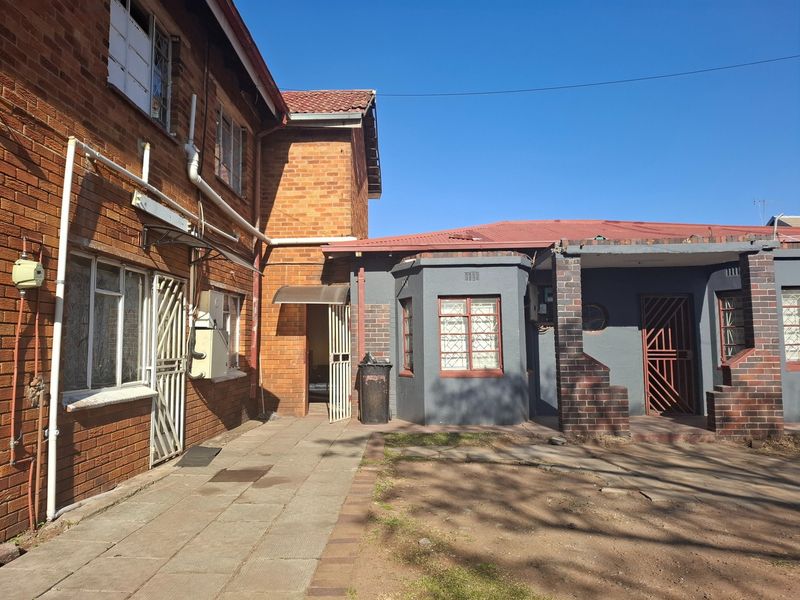 Rear exterior view of the property featuring a mix of face brick and painted walls, paved courtyard area, and secure metal entrance gates.