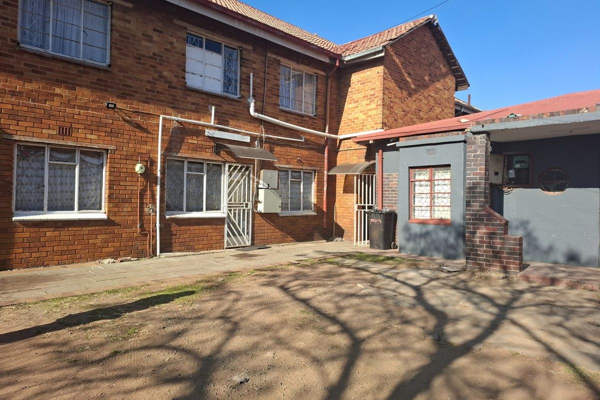 Rear view of a brick house featuring a paved patio area, security gates, and metal window frames.