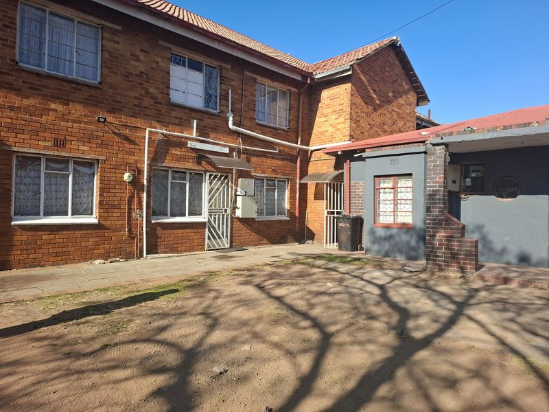 Rear view of a brick house featuring a paved patio area, security gates, and metal window frames.