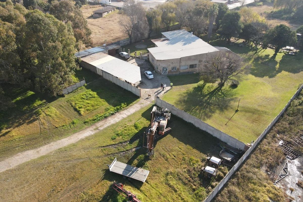 Aerial view of a small holding property featuring a main dwelling, outbuildings, perimeter fencing, and expansive grounds with visible maintenance requirements.