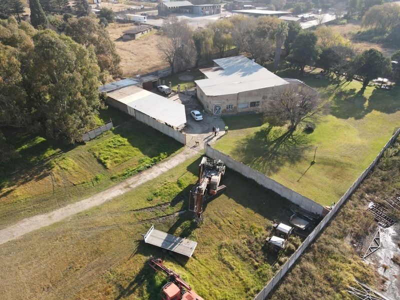 Aerial view of a small holding property featuring a main dwelling, outbuildings, perimeter fencing, and expansive grounds with visible maintenance requirements.