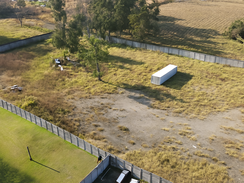 Aerial view of a large, fenced small holding plot featuring open grass areas and boundary walling.