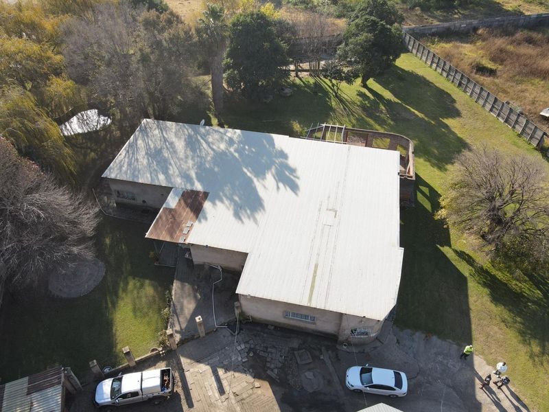 Aerial view of a small holding property featuring a large corrugated metal roof, expansive garden grounds, and a paved driveway area.
