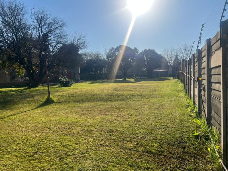 A spacious, well-maintained garden area featuring a large lawn, enclosed by a precast concrete boundary wall with integrated electric fencing.